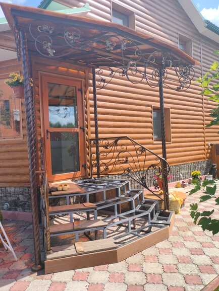 Кованое крыльцо с угловой лестницей и козырьком для бревенчатого дома